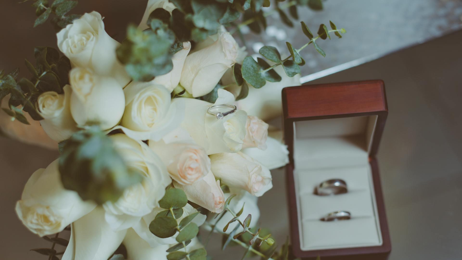 Silver wedding rings on jewelry display near a bouquet of roses